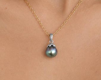 May include: A necklace featuring a round, dark iridescent pearl pendant suspended from a silver-toned bail. The pendant is attached to a delicate gold-toned chain that rests around the neck, showcasing a smooth, lustrous surface on the pearl.