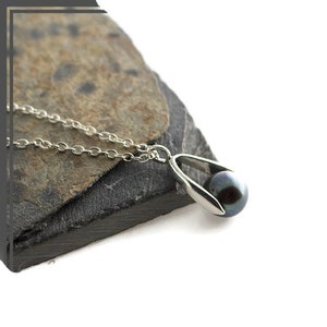 Pu&ograve; includere: Una collana d'argento con un ciondolo di perla nera. Il ciondolo ha la forma di una pinza che tiene la perla.