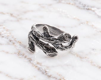 May include: A silver-toned ring featuring a textured design that mimics the appearance of intertwined tree branches. The metal surface has a dark, oxidized finish to highlight the bark-like details. The interior of the band is stamped with 925.