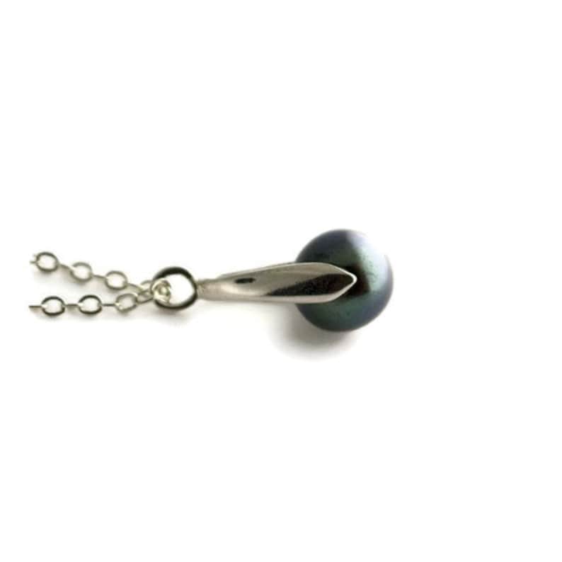 Pu&ograve; includere: Una collana a catena d'argento con un ciondolo di perla nera. Il ciondolo ha una chiusura argentata a forma di foglia.