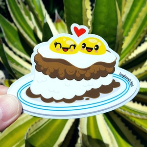 May include: A sticker featuring a cartoon illustration of a plate of food. The food consists of a stack of white rice, a layer of brown meat, and two sunny-side-up eggs with smiling faces. A red heart is above the eggs. The plate has blue stripes and the text "tinyhearts808".