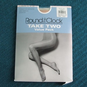 May include: A rectangular package of Round the Clock Take Two value pack control top pantyhose. The packaging features a black and white graphic of legs and text including Style 614, Pale Beige, Size A, and Ultra Sheer Leg. The background is white.