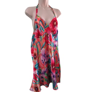 Può includere: Un vivace abito all'americana con stampa floreale nei toni del rosso, rosa, viola e verde acqua. L'abito presenta uno scollo a V e una gonna fluida fino al ginocchio. Il tessuto sembra essere un materiale setoso, perfetto per il clima caldo o le occasioni speciali.