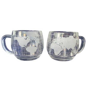 May include: Two clear glass mugs with a world map etched on the side. The mugs have a handle and are perfect for enjoying a hot beverage.
