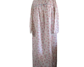 Puede incluir: Un camisón blanco con estampado floral rosa y ribete azul alrededor del cuello y los puños. El camisón tiene un cierre de botones en la parte delantera y manga larga.