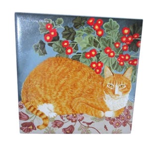 Puede incluir: Azulejo de cerámica cuadrado con un gato naranja con marcas blancas, descansando sobre una superficie floral. Flores rojas y hojas verdes en el fondo. El azulejo tiene un acabado brillante y el nombre del artista, Mimi Vang Olsen, está en la esquina superior izquierda.