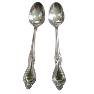 May include: Two silver spoons with a Christmas tree design on the handle. The spoons are polished and shiny.