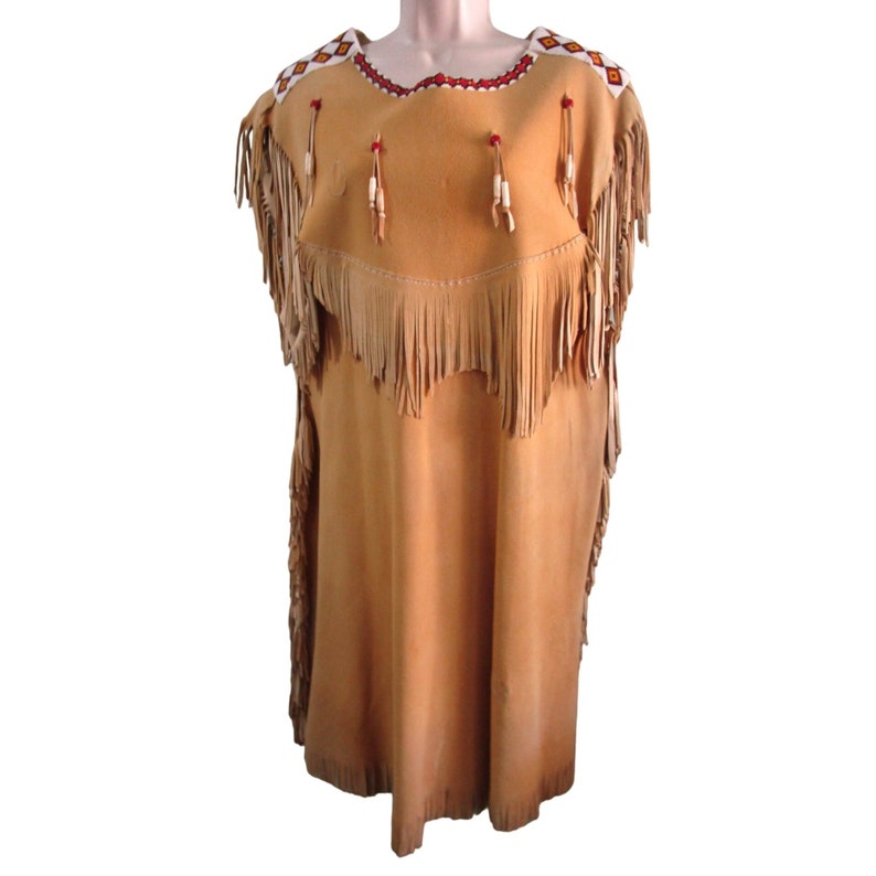 Puede incluir: Un vestido de cuero marr&oacute;n claro con detalles de flecos y adornos de cuentas. El vestido tiene un escote redondo y es sin mangas.