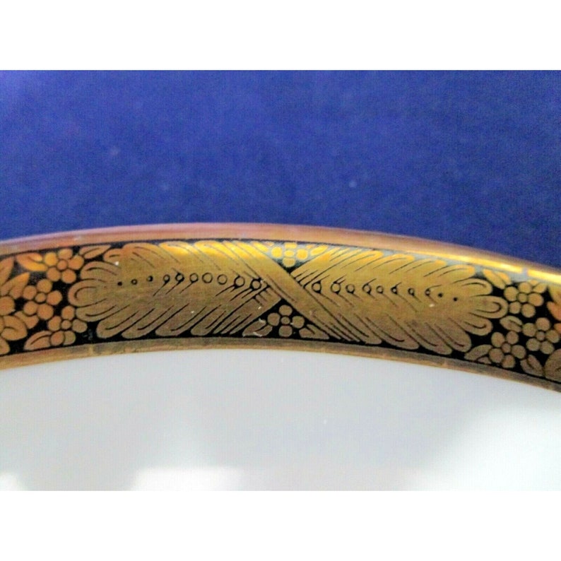 Op de afbeelding: Een wit keramiek bord met een zwarte en gouden rand. De rand heeft een gestileerd bloemmotief met gouden accenten.