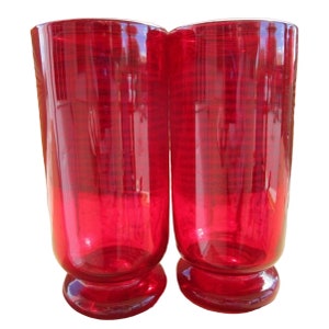 May include: Two red glass tumblers with a rounded base. The glasses are clear and have a slightly rippled texture.