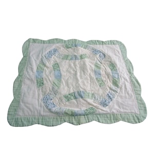 May include: A handmade quilt with a Double Wedding Ring pattern. The quilt has a white central area with a floral design, encircled by rings of blue and green fabric. The edges are scalloped with a green border.