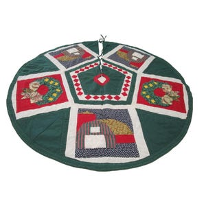 May include: A green, red, white, and yellow patchwork quilted Christmas tree skirt with a wreath design.
