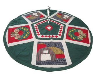 May include: A green, red, white, and yellow patchwork quilted Christmas tree skirt with a wreath design.
