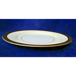 Op de afbeelding: Een wit keramiek dinerbord met een gouden rand. Het bord heeft een kleinere witte cirkel in het midden met een dunne gouden rand.