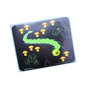 May include: A sticker with a black background featuring a neon green centipede-like creature, mushrooms, and a dragon. A red dotted line and a spider-like insect are also present. The text "PRINTED IN U.S.A." is printed at the bottom.