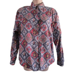 Puede incluir: Una camisa de manga larga con botones, fondo azul y un estampado geométrico colorido con detalles en rojo, amarillo y marrón. El estampado incluye caballos estilizados y motivos florales.