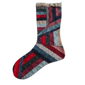 Puede incluir: Una media de Navidad de patchwork con un esquema de color rojo, azul y verde. La media está hecha de varias telas con diferentes patrones, incluyendo flores y cuadros.