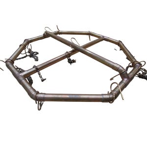 Op de afbeelding: Een achtkantig frame van koperkleurig metaal met acht haken en twee dwarsbalken. Het frame is ontworpen om items aan de haken te hangen.