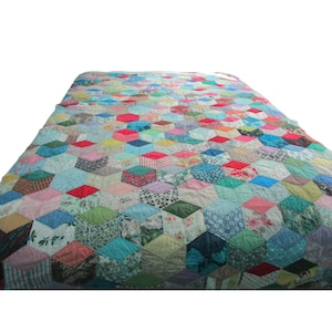 May include: A colorful quilt with a geometric pattern of hexagonal shapes. The quilt features a variety of fabrics in shades of blue, pink, red, green, and yellow. The quilt is likely handmade and has a vintage aesthetic.
