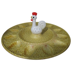May include: A yellow ceramic serving dish with a woven pattern and six individual sections. A white ceramic rooster figurine with a red comb sits in the center of the dish.