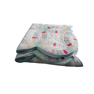 May include: Folded vintage quilt with a white background and colorful patchwork design. The quilt features a light blue border and a pattern of interlocking circles and rectangles in shades of pink, green, and yellow.