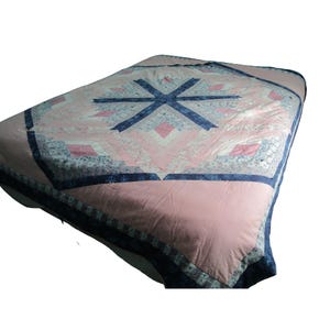 May include: A pink and blue quilt with a geometric starburst design in the center. The quilt features a pink background with blue and white patterned accents and a dark blue border. The quilt is likely for a bed.