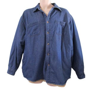 Peut inclure: Une chemise en jean bleu avec un col, deux poches de poitrine et des boutons. La chemise a des manches longues et une doublure en sherpa. La chemise est présentée sur un mannequin.
