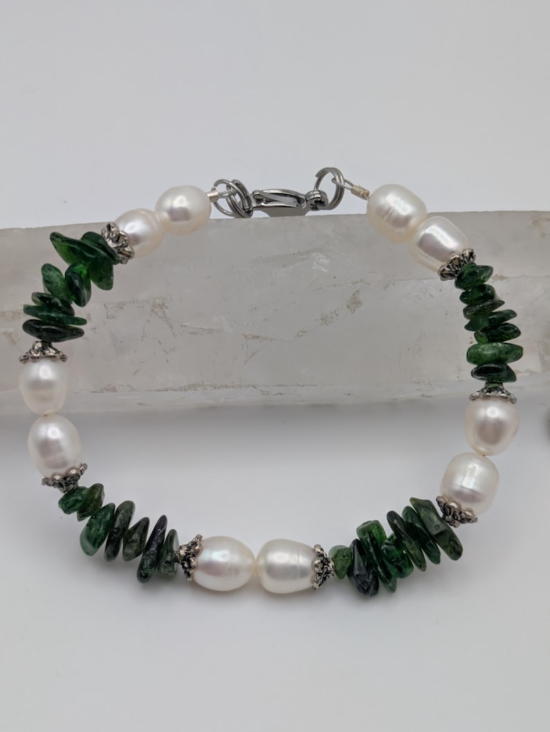 Op de afbeelding: Een armband gemaakt met witte parels en groene edelsteen chips. De armband heeft een zilveren sluiting.