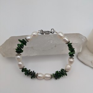 Op de afbeelding: Een armband met witte parels en groene edelsteen kralen. De armband heeft een zilveren sluiting.