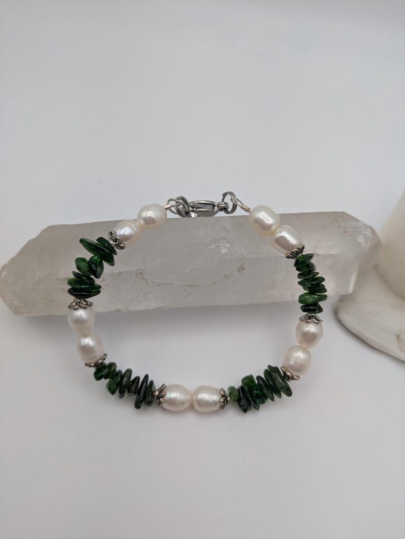Op de afbeelding: Een armband met witte parels en groene edelsteen kralen. De armband heeft een zilveren sluiting.