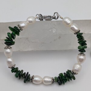 Op de afbeelding: Een armband gemaakt met witte parels en groene edelsteen chips. De armband heeft een zilveren sluiting.