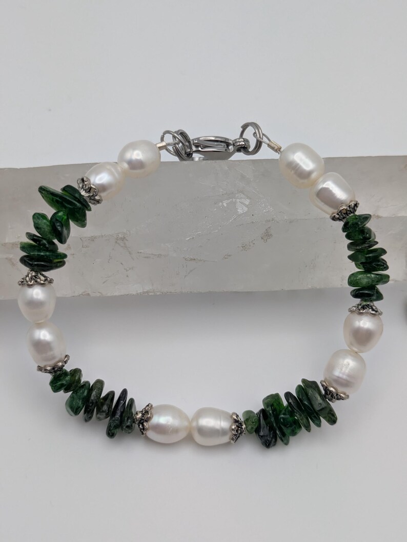 Op de afbeelding: Een armband gemaakt met witte parels en groene edelsteen chips. De armband heeft een zilveren sluiting.