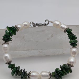 Op de afbeelding: Een armband gemaakt met witte parels en groene edelsteen chips. De armband heeft een zilveren sluiting.