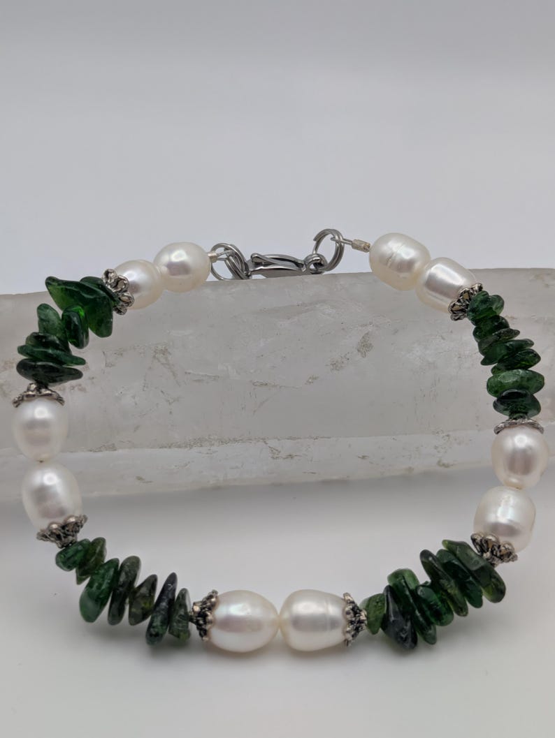 Op de afbeelding: Een armband gemaakt met witte parels en groene edelsteen chips. De armband heeft een zilveren sluiting.