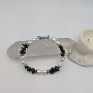 Op de afbeelding: Een armband gemaakt van witte parels en groene jade-chips. De armband heeft een zilveren sluiting.