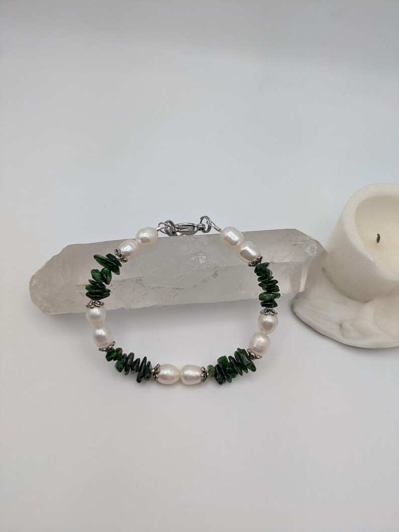 Op de afbeelding: Een armband gemaakt van witte parels en groene jade-chips. De armband heeft een zilveren sluiting.