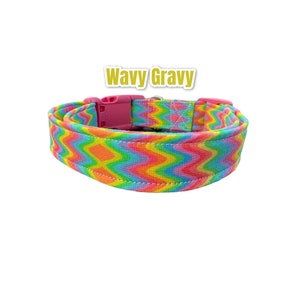 Pode incluir: Uma coleira de cachorro colorida com uma fivela rosa. A coleira tem um padrão ondulado em tons de rosa, laranja, amarelo, verde e azul. O texto "Wavy Gravy" está impresso em letras douradas acima da coleira.