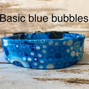 May include: A blue and white dog collar with a pattern of blue circles and white dots. The collar has a white stitching detail and the text "Basic blue bubbles" is visible above the collar.