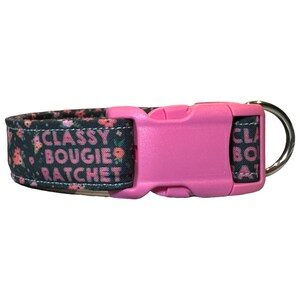 May include: A black dog collar with a pink floral print and the text "CLASSY BOUGIE RATCHET". The collar has a pink plastic buckle and a silver metal D-ring.