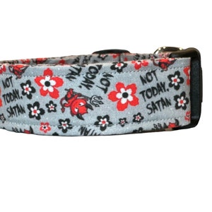 May include: A gray dog collar with a black buckle and a red and black floral pattern. The collar has the text "Not Today, Satan" printed on it.