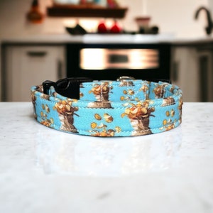 May include: A blue dog collar with a pattern of brown dogs and yellow coins. The collar is made of fabric and has a black plastic buckle.
