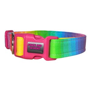 A rainbow-striped fabric dog collar with a pink plastic buckle that reads "TRIXIE ROX DESIGNS" is shown on a white background.