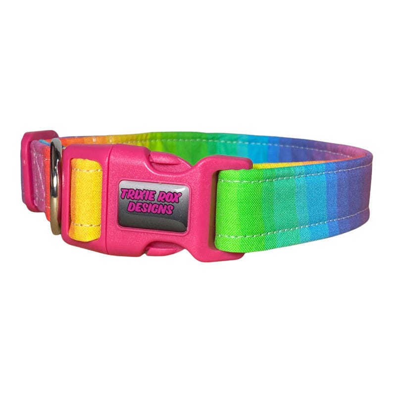 A rainbow-striped fabric dog collar with a pink plastic buckle that reads "TRIXIE ROX DESIGNS" is shown on a white background.