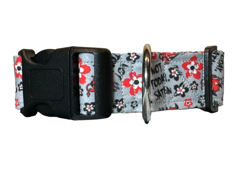 May include: A gray dog collar with a black buckle and silver ring. The collar has a floral pattern with red flowers and the text "Not Today, Satan".