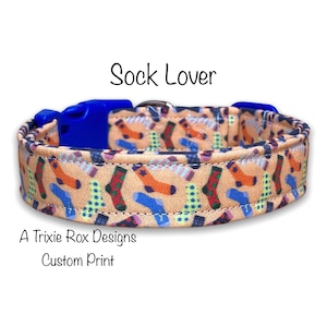 May include: A tan dog collar with a blue buckle and a colorful print of socks. The collar is labeled "Sock Lover" and "A Trixie Rox Designs Custom Print".