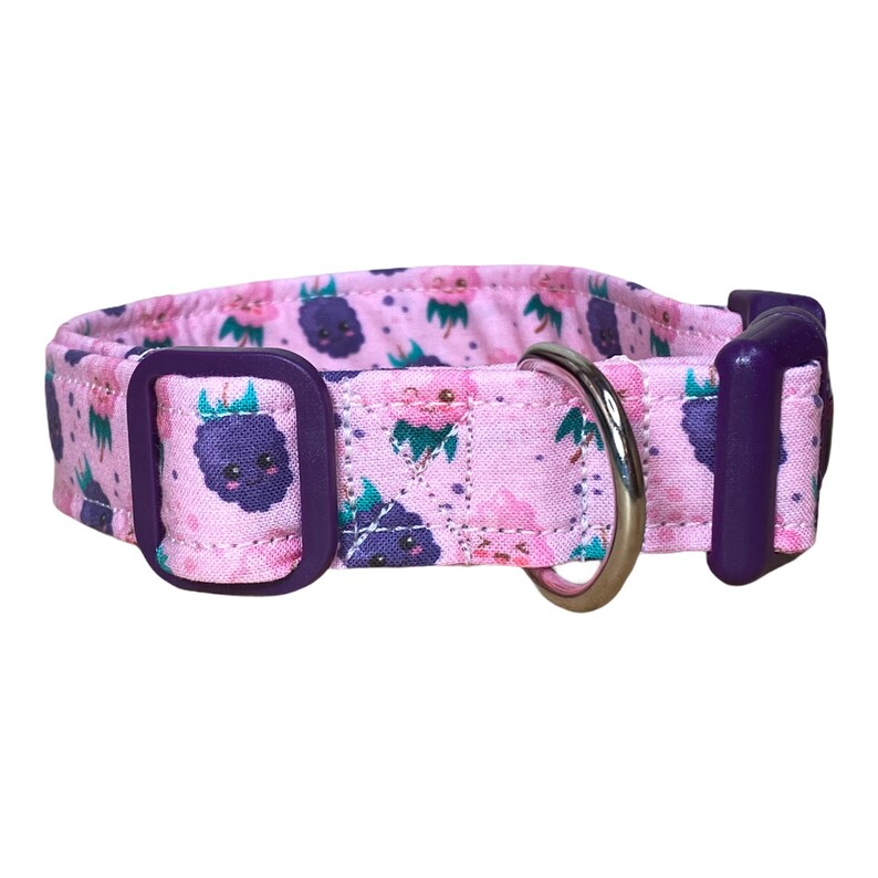 May include: A pink dog collar with a purple buckle and a silver D-ring. The collar has a pattern of purple cartoon blackberries with happy faces on a pink background.
