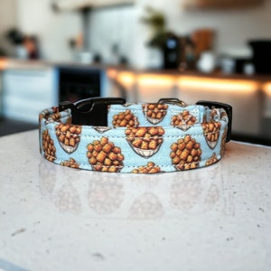 May include: A light blue dog collar with a repeating pattern of brown and white fried chicken nuggets in a white paper bowl.