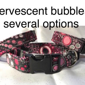 May include: Three black and pink dog collars with a white and grey polka dot pattern. The collars have black plastic buckles.