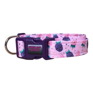 May include: Purple and pink dog collar with a repeating pattern of cartoon blueberries and flowers. The collar has a purple buckle with the text "TRIXIE ROX DESIGNS" on it.