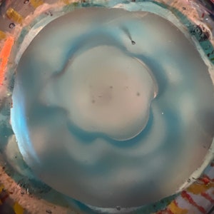 May include: A close-up of a blue glass bottle with a textured surface. The bottle has a clear, round opening at the top.